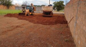 Retroescavadeira e um caminhão efetuando o serviço de terraplanagem.